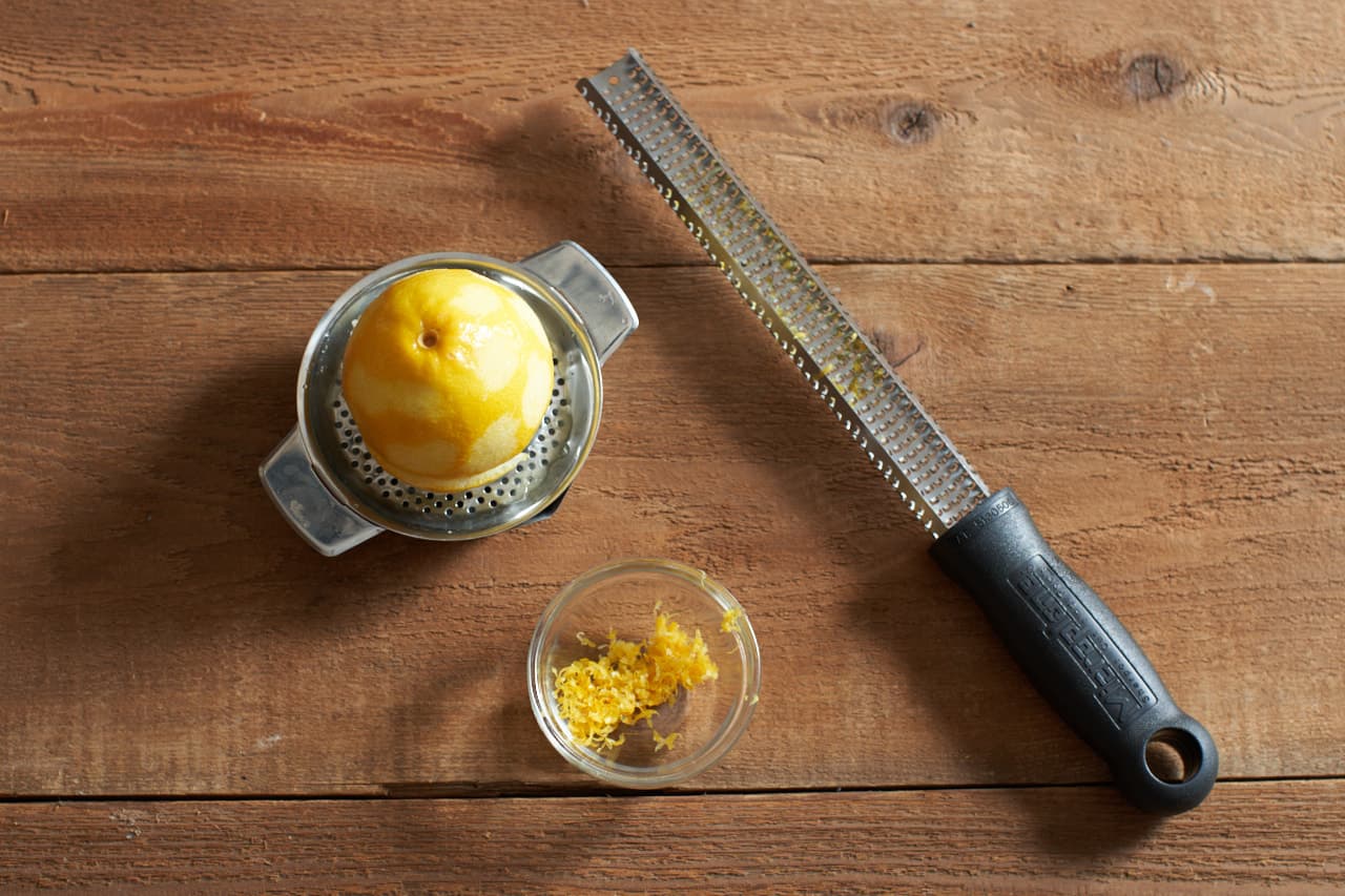 Half a lemon on a juicer, a small bowl of lemon zest, and a microplane grater.