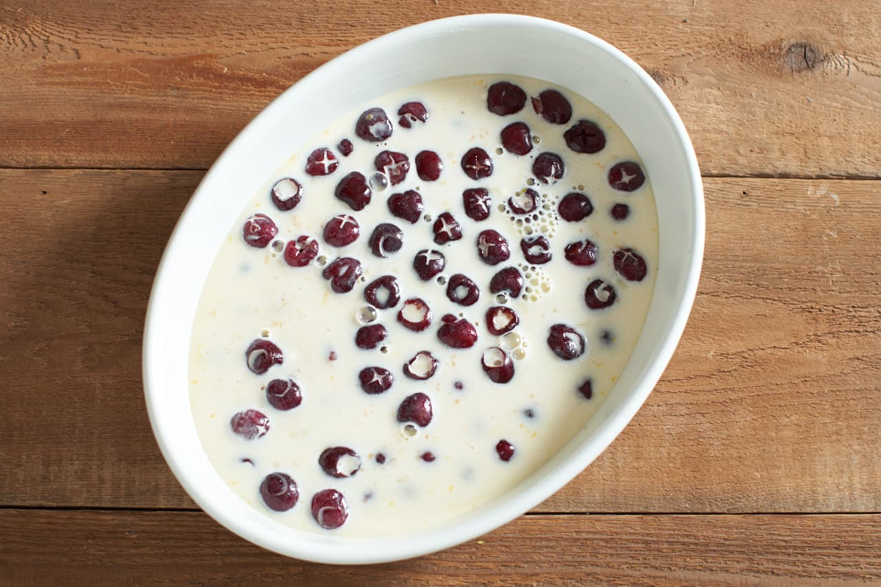 Clafoutis batter and cherries in an oval baking dish.