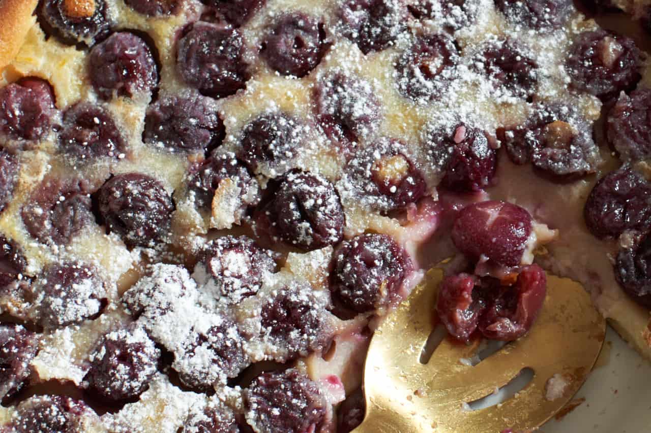 Closeup of cherry clafoutis topped with powdered sugar with a gold spoon placed where a serving has been scooped out.