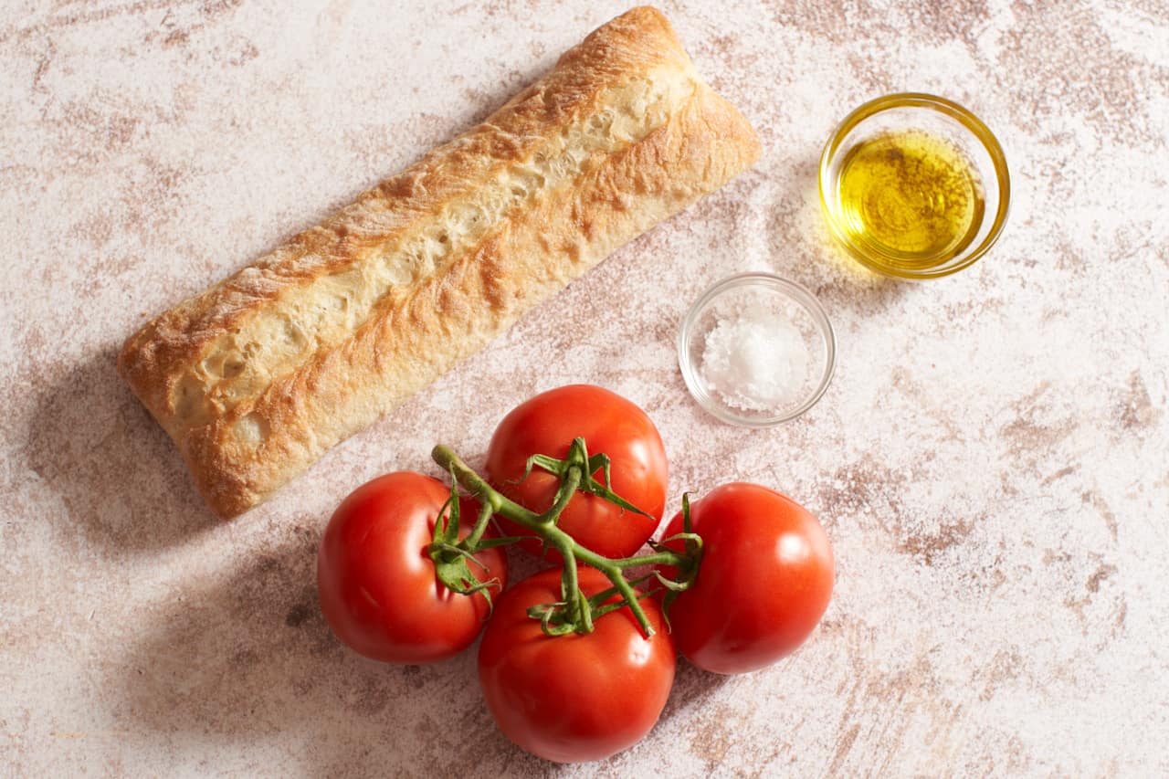 Ciabatta bread, tomatoes on the vine, and two small bowls of olive oil and sea salt.