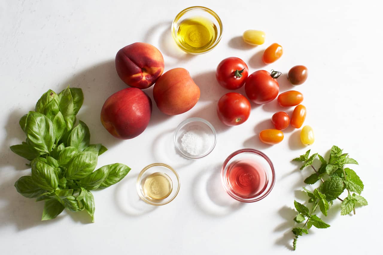 Tomatoes, nectarines, fresh basil and mint, alongside small glass bowls with honey, salt, red wine vinegar and olive oil.