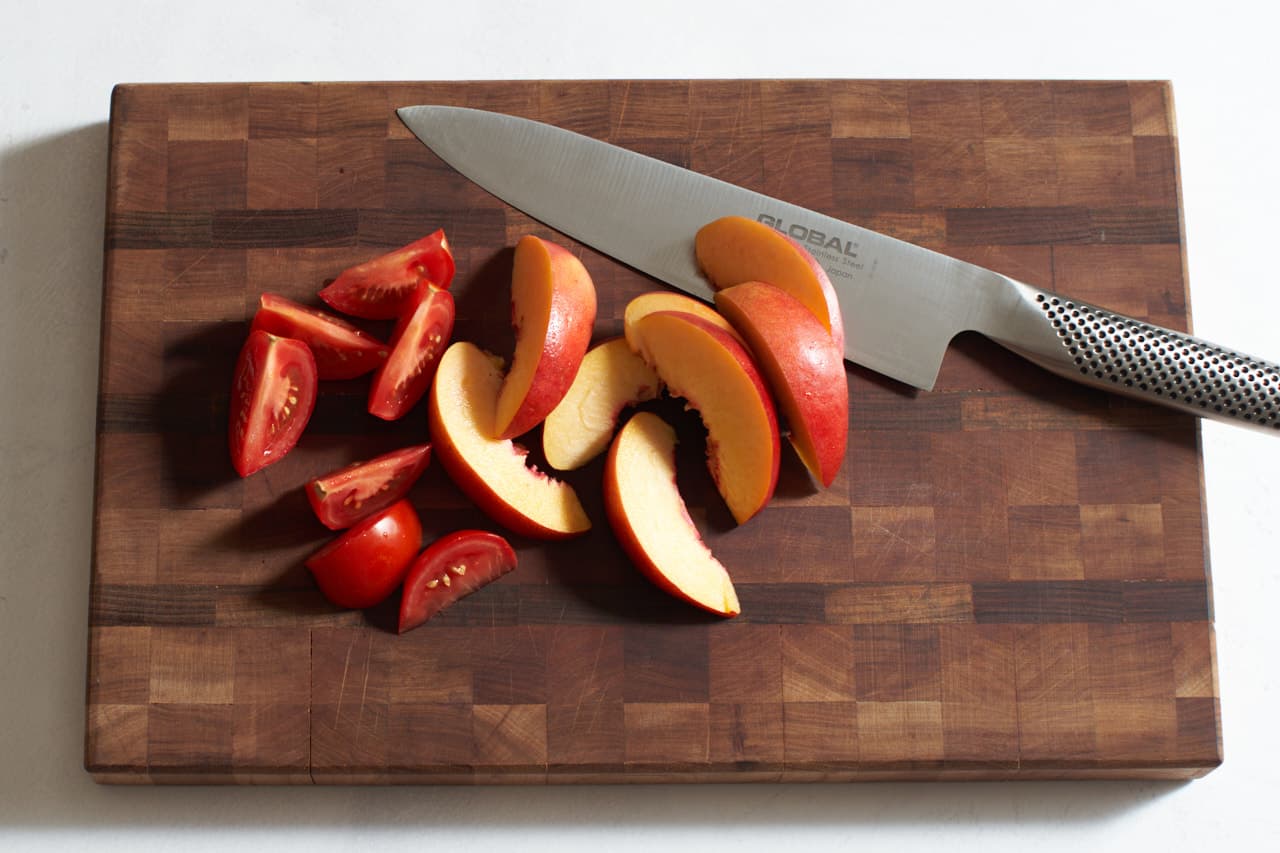 A knife on a cutting board with sliced nectarines and tomatoes.