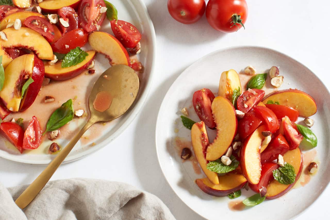 Two plates of nectarine salad with tomatoes, one has a gold spoon on it.