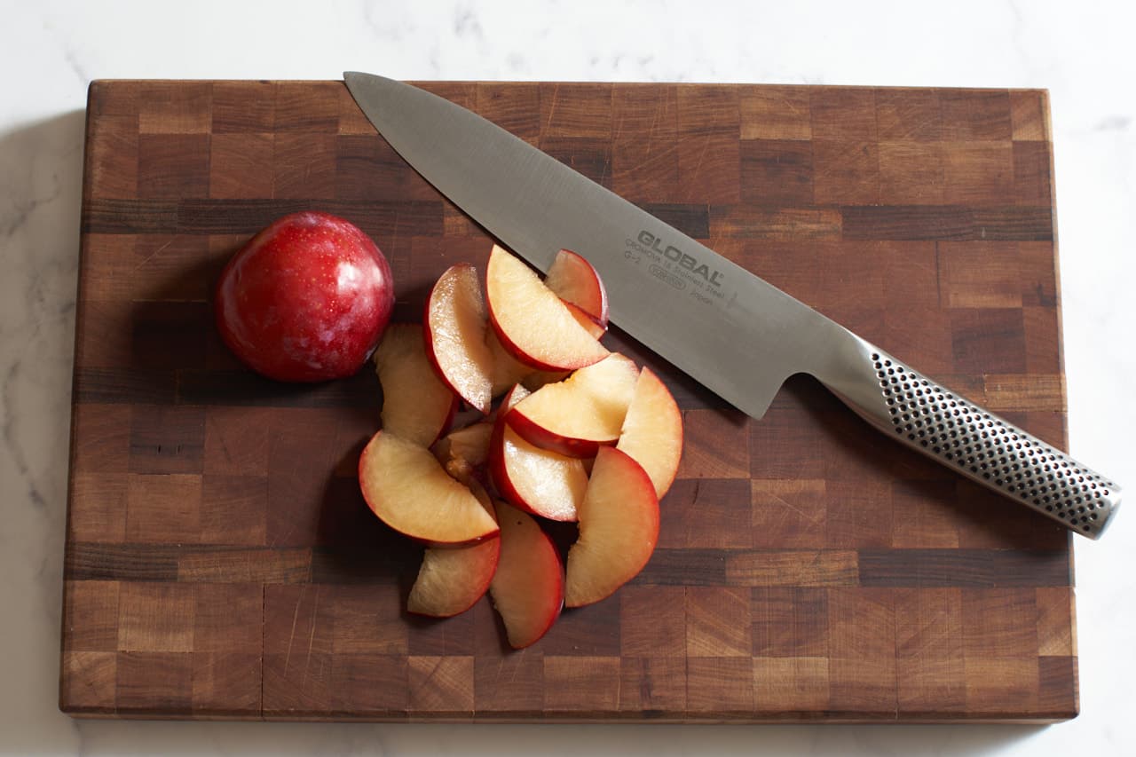 A knife on a wooden cutting board with sliced plums.