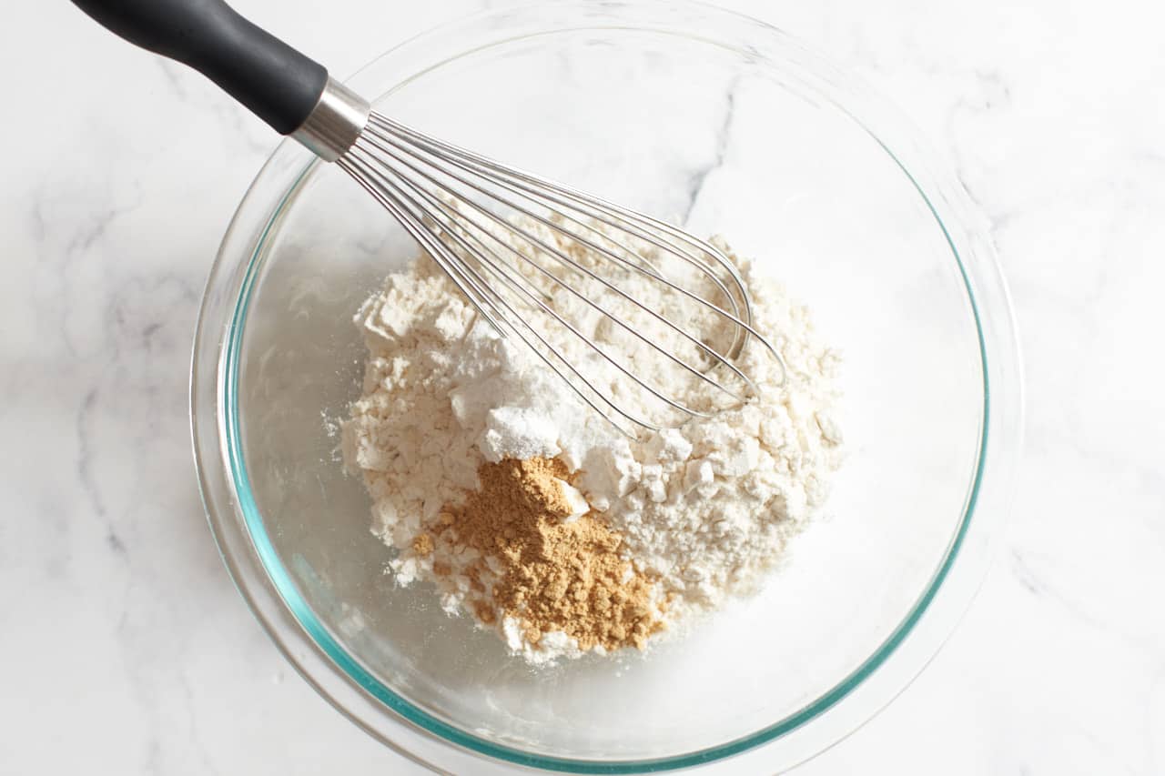 A bowl of dry ingredients for cake with a whisk in it.