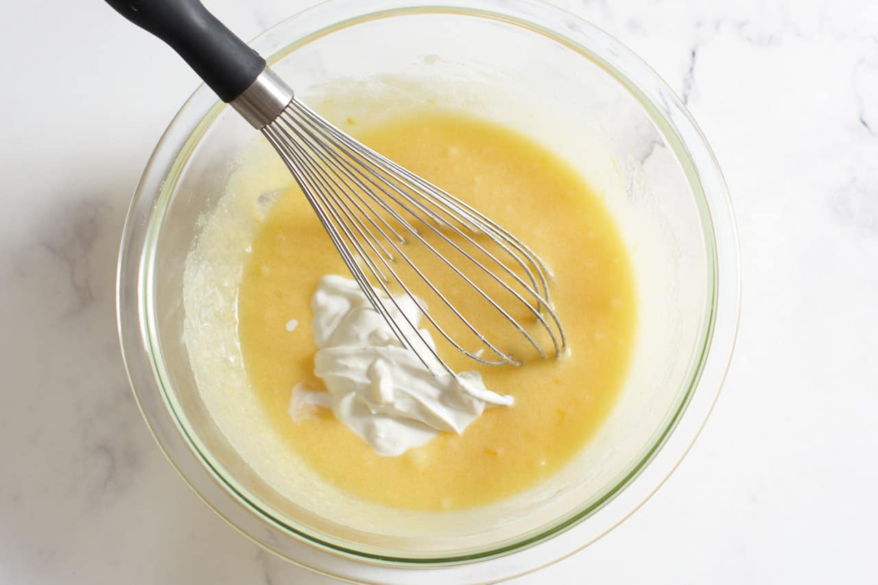 Yogurt added to the liquid ingredients of cake batter in a bowl with a whisk.