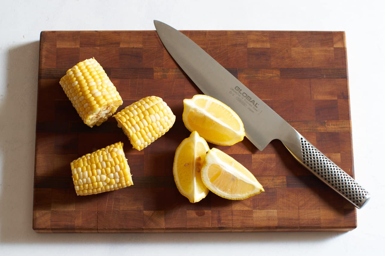 A knife on a cutting board with lemon wedges and pieces of corn on the cob.