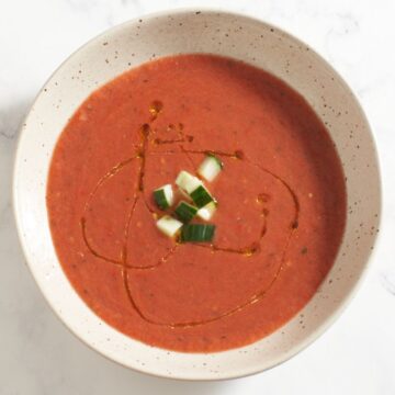 Top down view of a bowl of gazpacho topped with chopped cucumber and a drizzle of olive oil.
