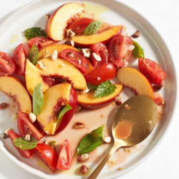 A plate of nectarine salad with tomatoes and herbs, a gold spoon is on the right side of the plate.