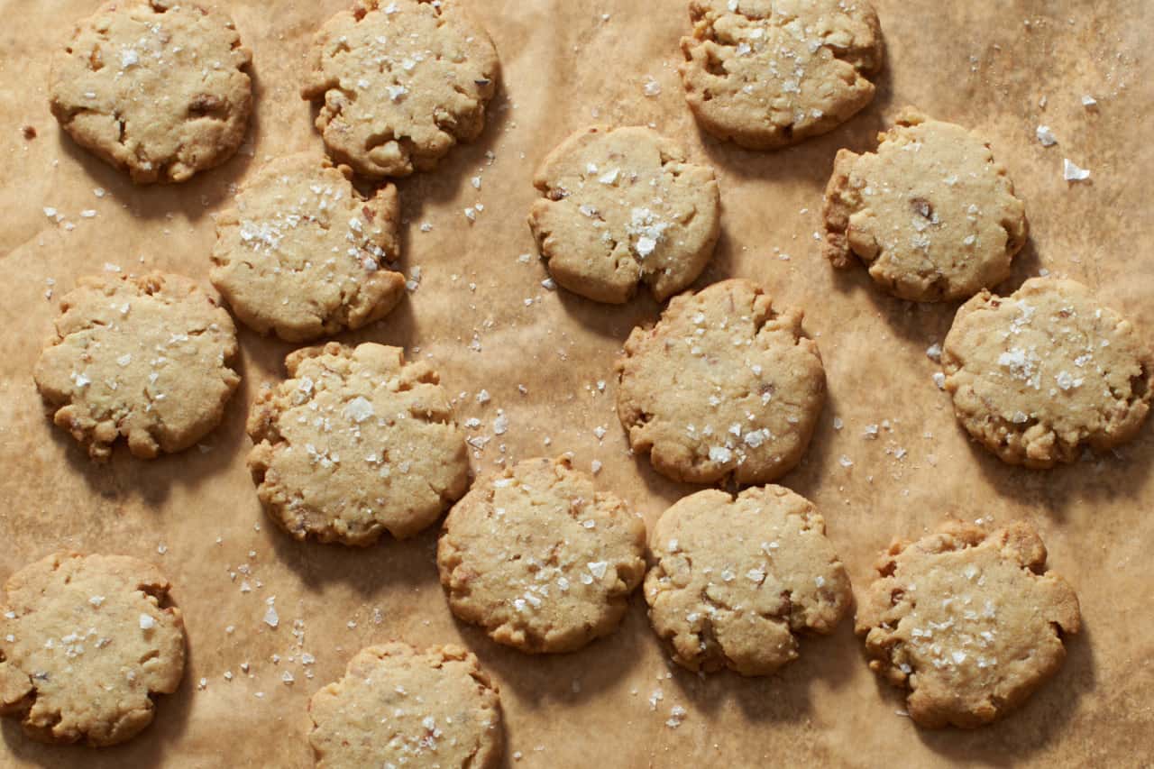Pecan sandies cookies topped with flaky sea salt on brown parchment paper.
