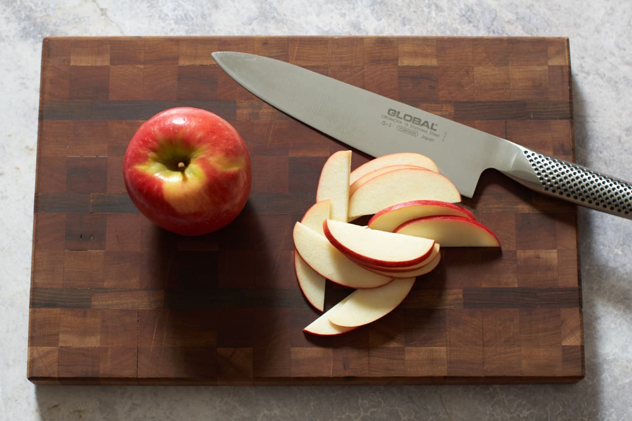 A knife on a cutting board with thin slices of apple.
