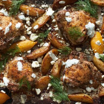 Greek chicken and potatoes with feta, yogurt sauce and fresh dill on a sheet pan.