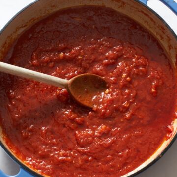 Homemade tomato sauce in a blue pan with a wooden spoon.