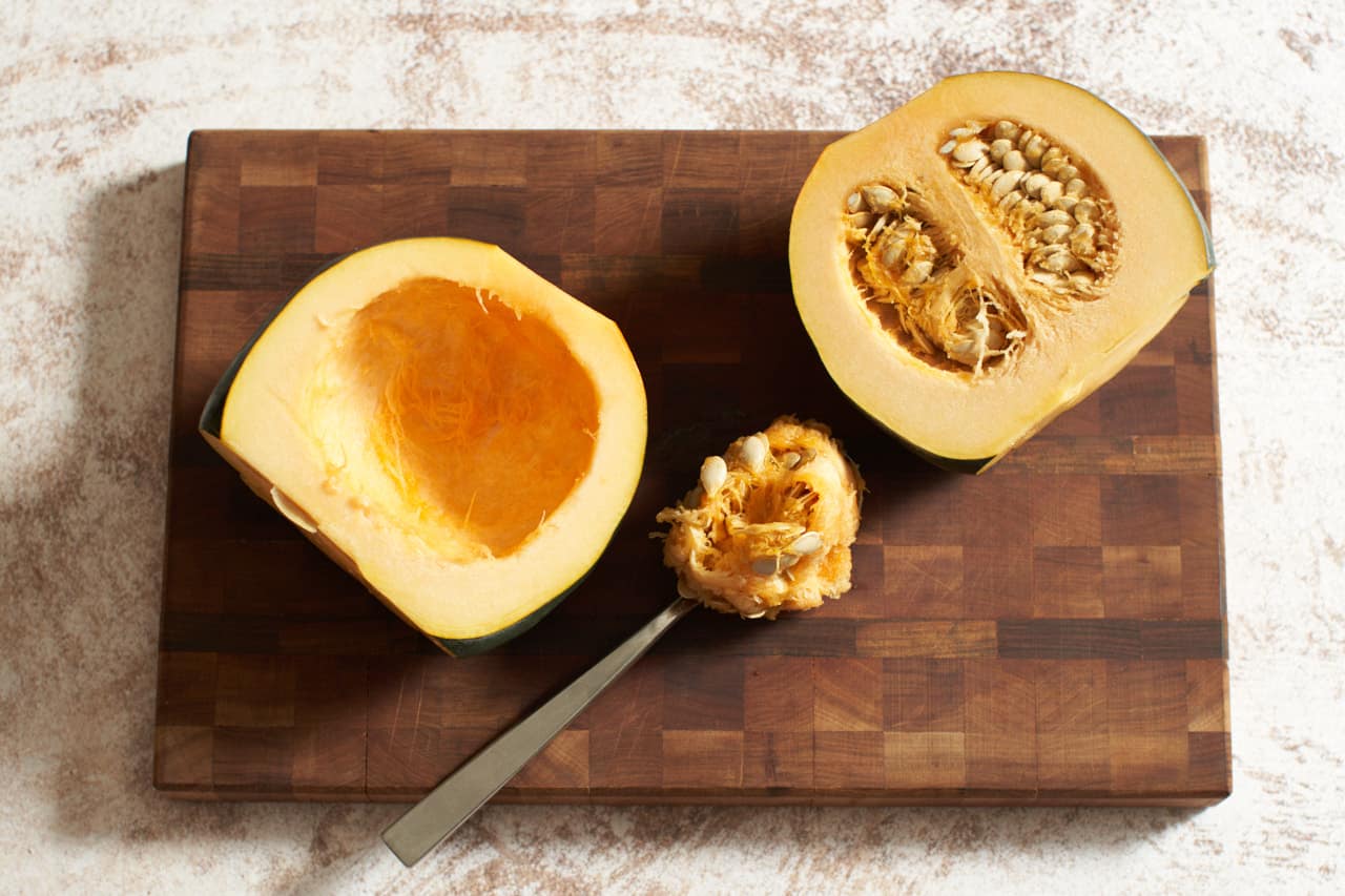Two acorn squash halves, one without seeds. A spoon full of squash seeds is between them.