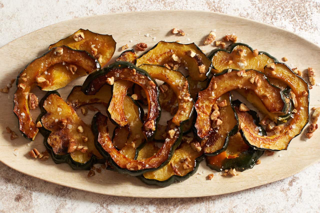 An oval plate of maple roasted acorn squash topped with pecans and flaky sea salt.