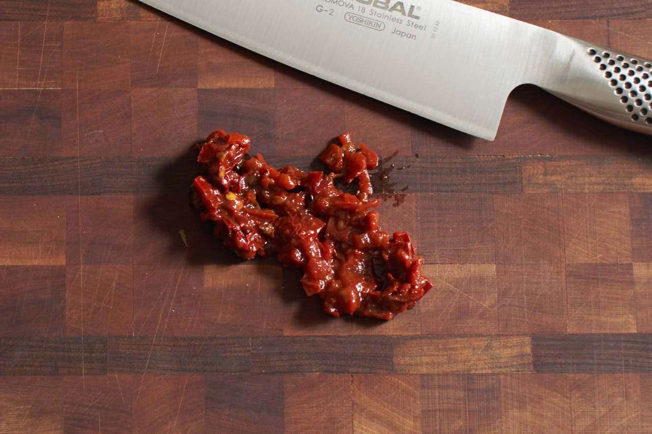 Finely chopped chipotle peppers on a cutting board with a knife.