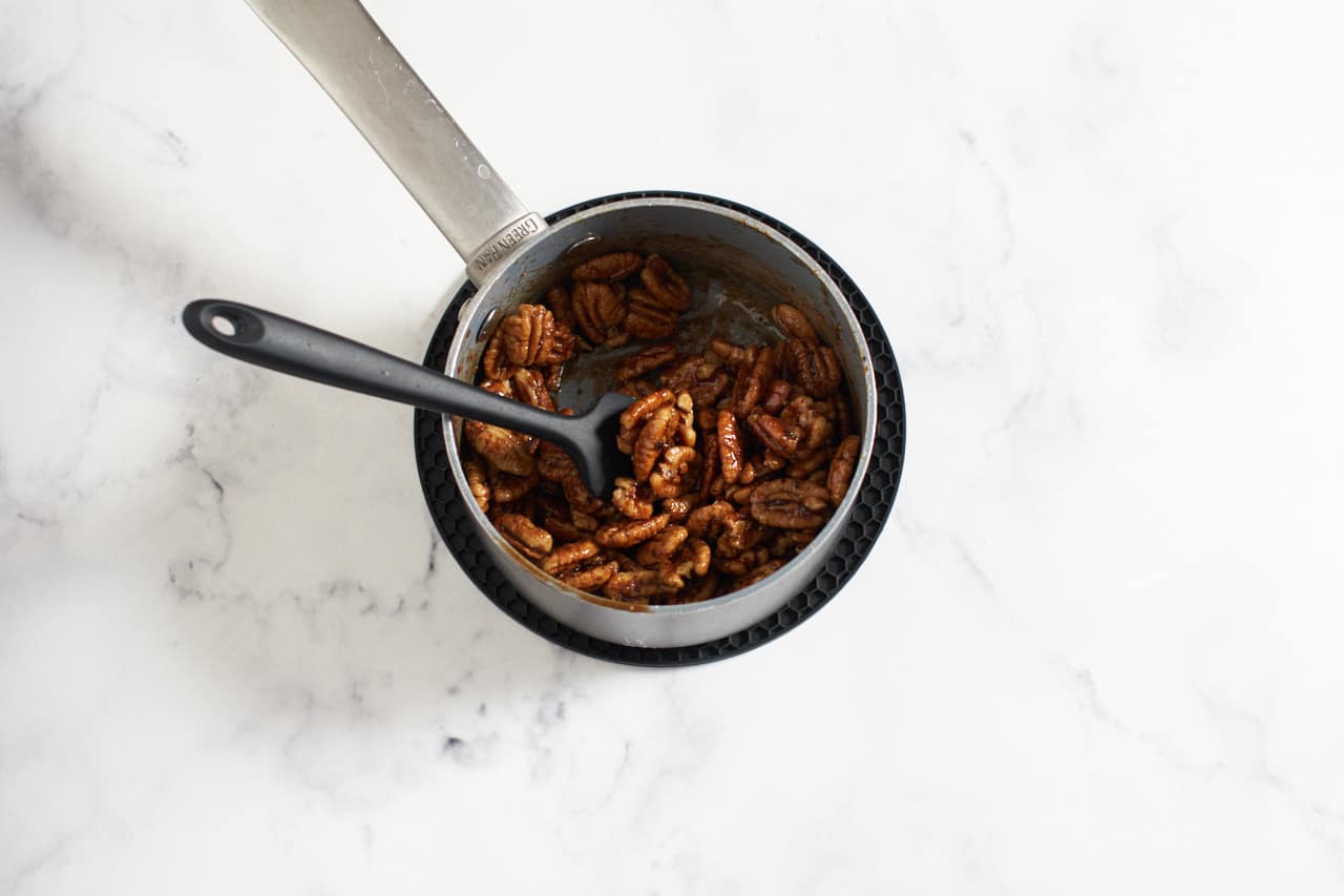 Candied pecans in a small sauce pan with a black spatula in it.