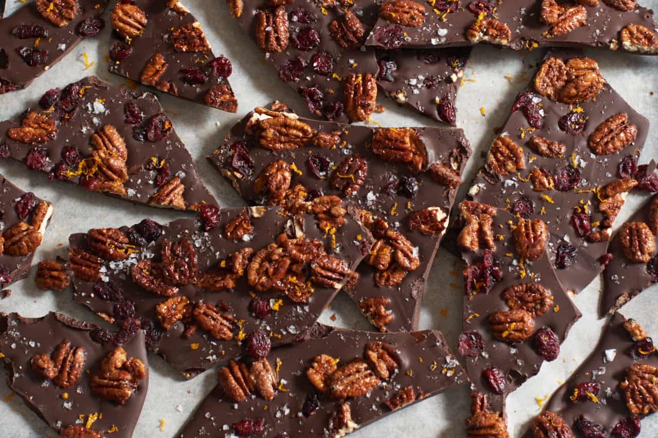 Pieces of cranberry pecan dark chocolate bark on white parchment paper.