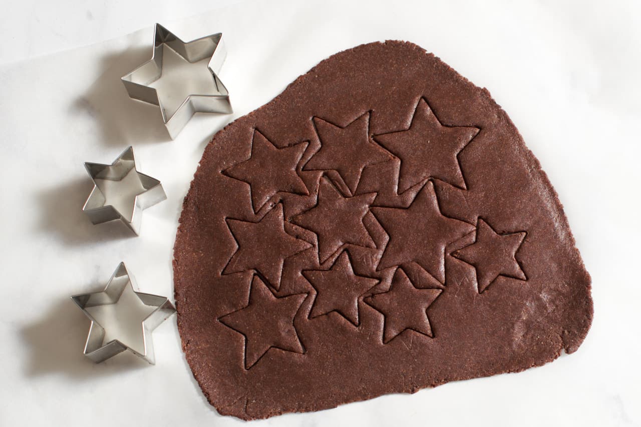 Cookie dough with star shapes pressed into it. Three star cookie cutters are to the left.