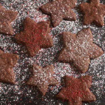 Basler brunsli cookies cut into star shapes of various sizes, topped with powdered sugar and red sanding sugar.