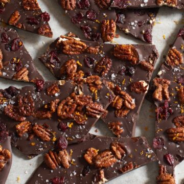Pieces of cranberry pecan dark chocolate bark on white parchment paper.