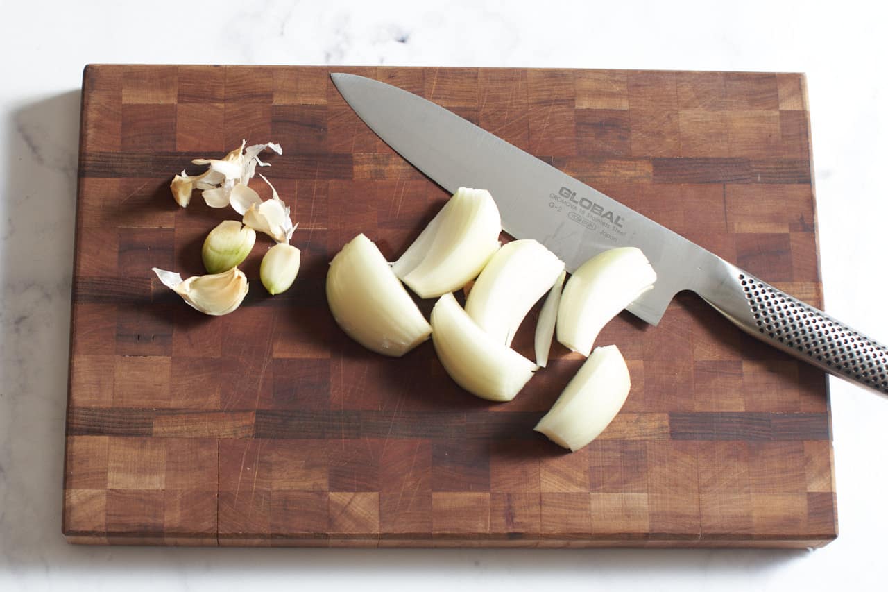 Smashed garlic and onion slices on a cutting board with a knife.