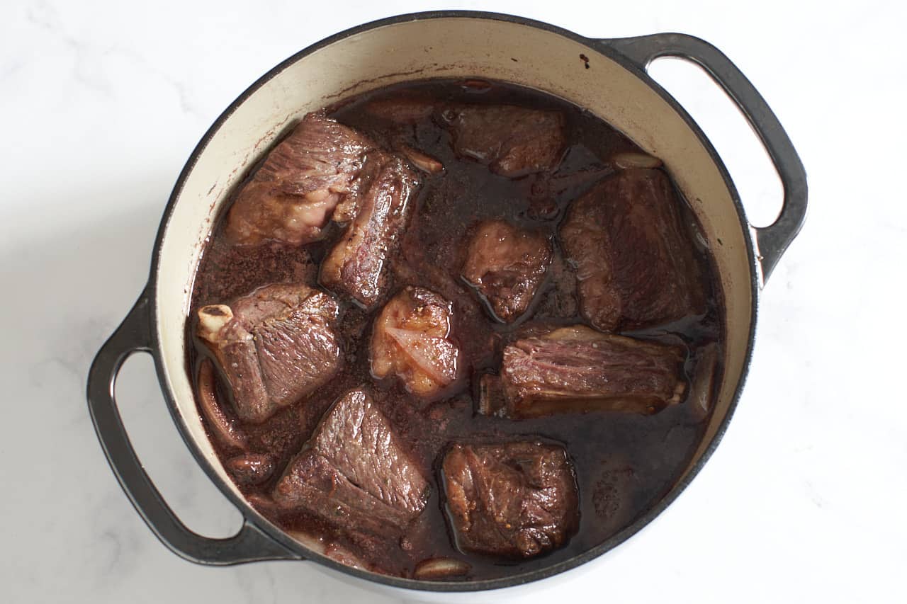 Short ribs in a pomegranate wine sauce ready to braise in a Dutch oven.