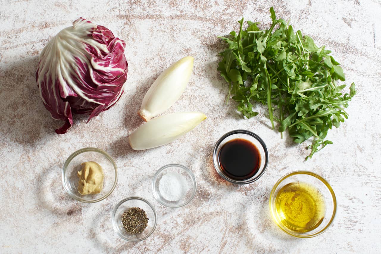 Radicchio, endive, and arugula next to small bowls of balsamic vinegar, dijon mustard, salt, pepper, and olive oil.