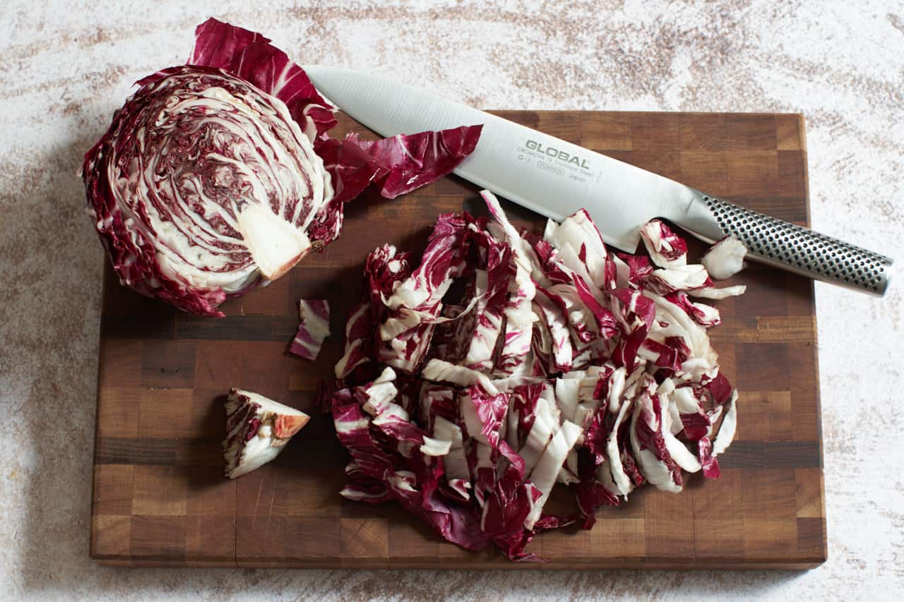 A head of radicchio sliced in half and chopped on a cutting board with a knife.