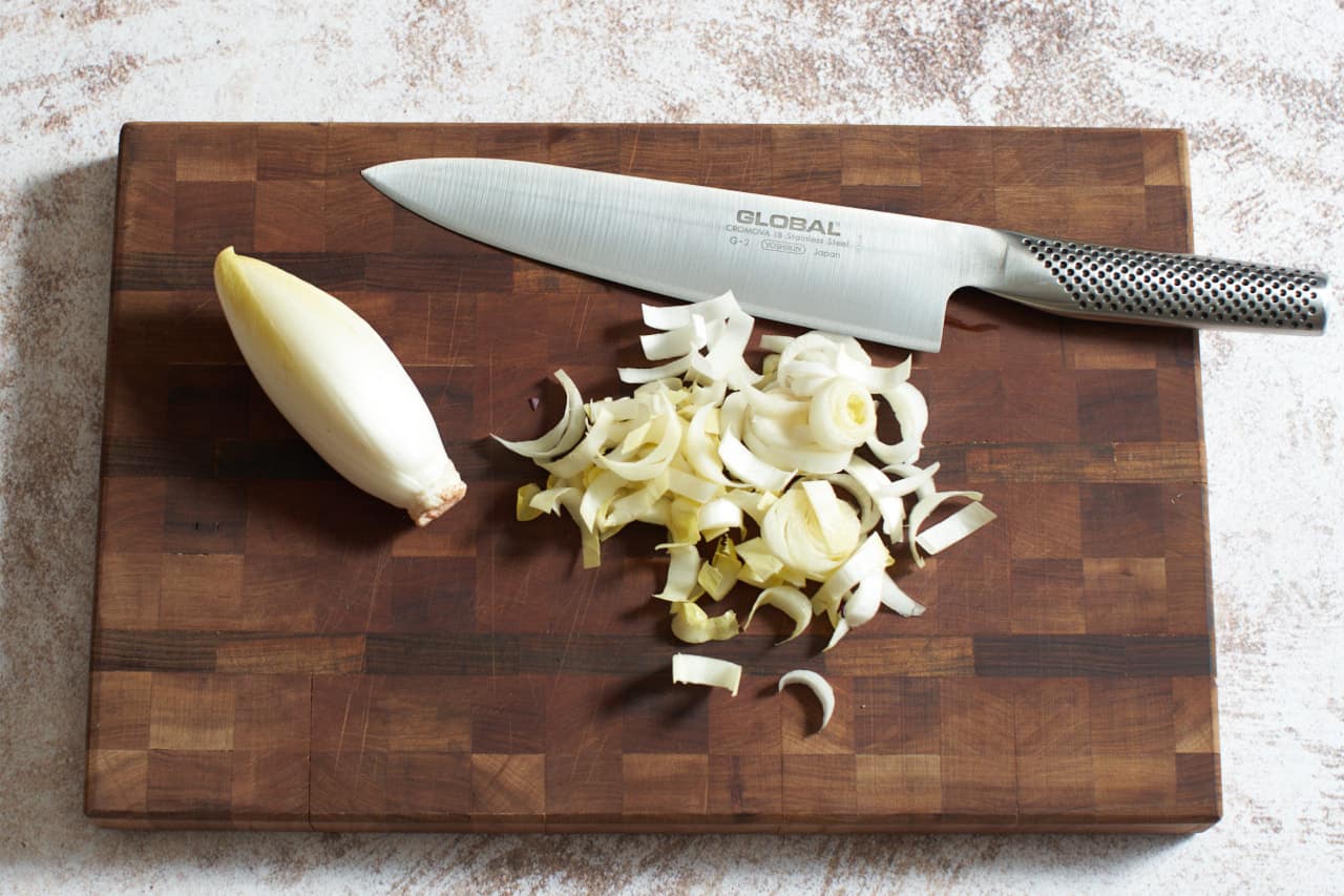 An endive and chopped endive on a cutting board with a knife.