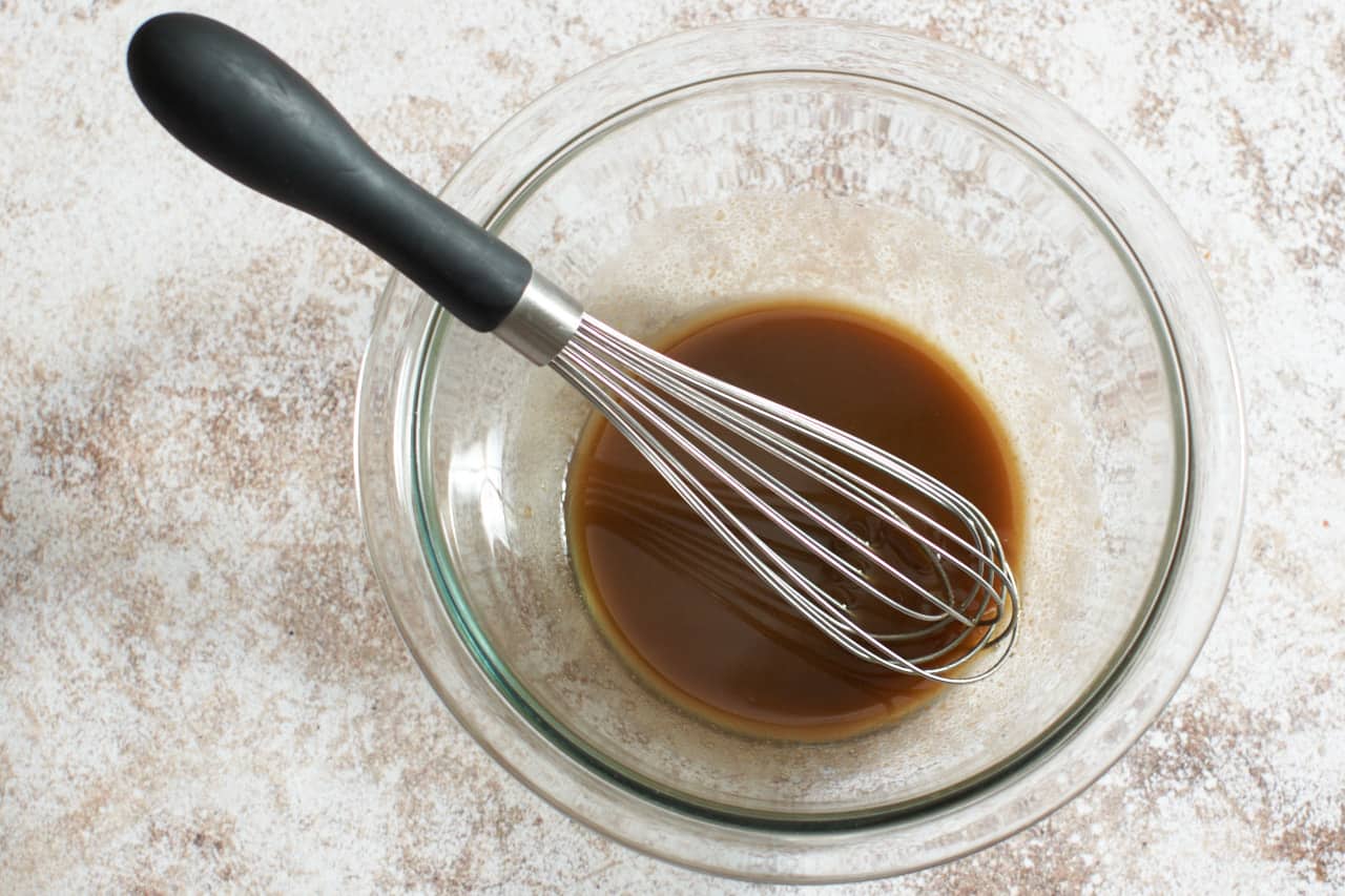 A glass bowl of balsamic vinaigrette with a whisk in it.