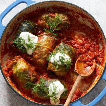 Holubtsi—Ukranian cabbage rolls—topped with sour cream and fresh dill in a round pan. A wooden spoon is on the right.