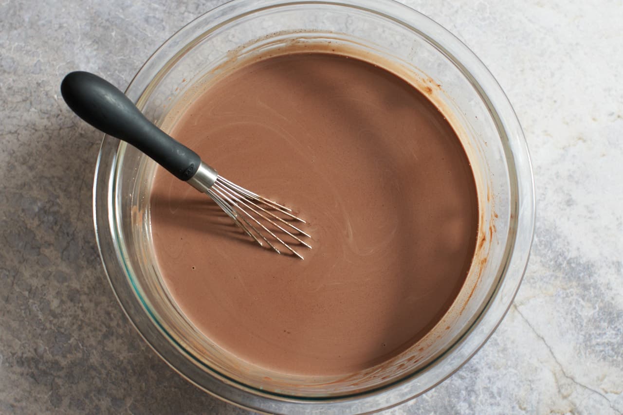 A bowl of melted chocolate and heavy cream with a whisk in it.
