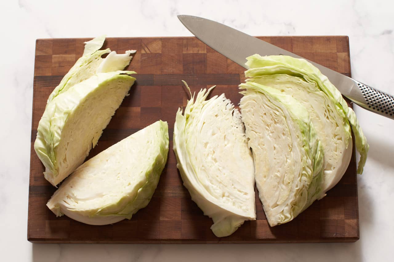 Half a cabbage sliced into wedges on a cutting board with a knife.