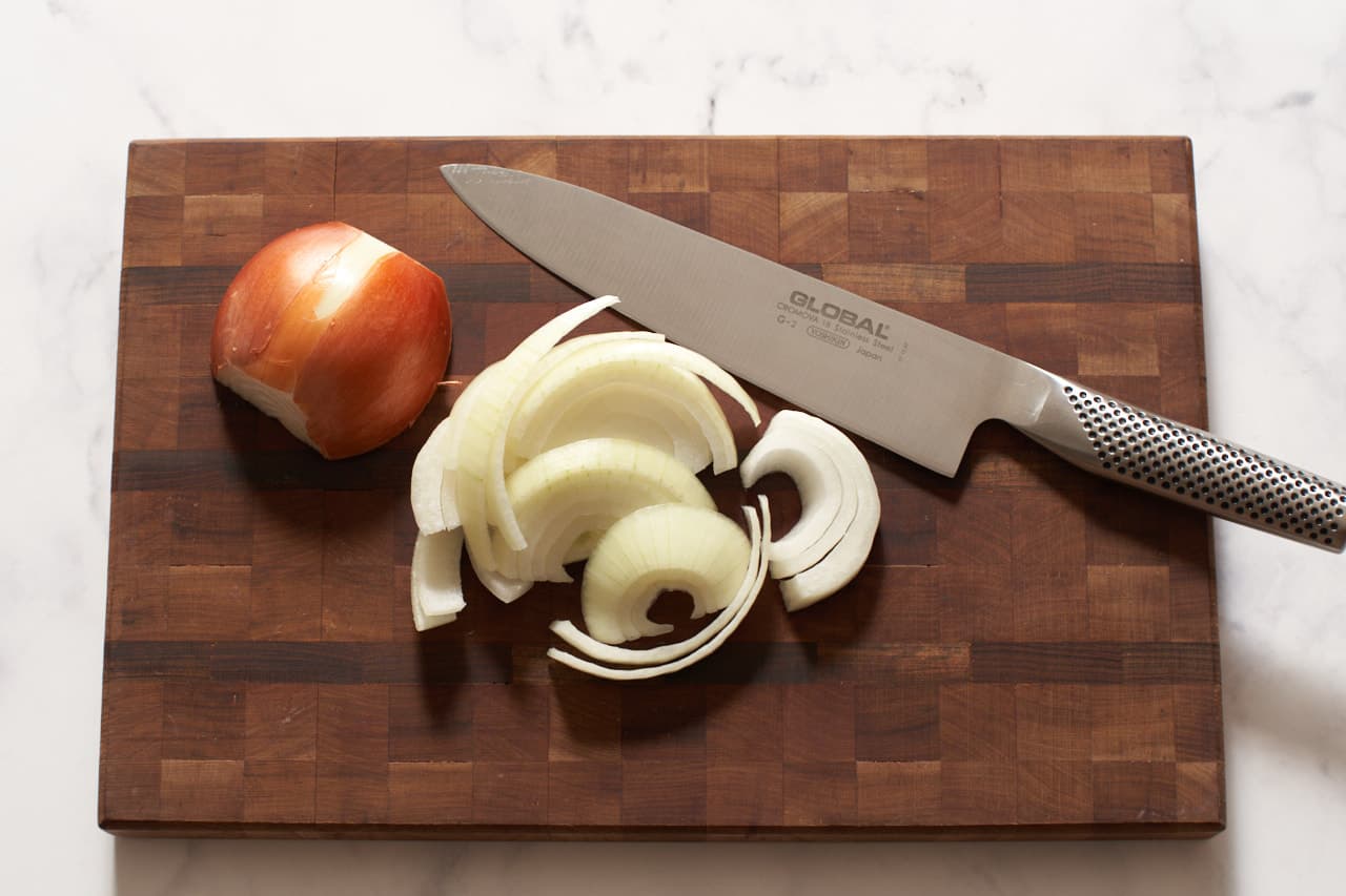 An onion cut into slices on a cutting board with a knife.
