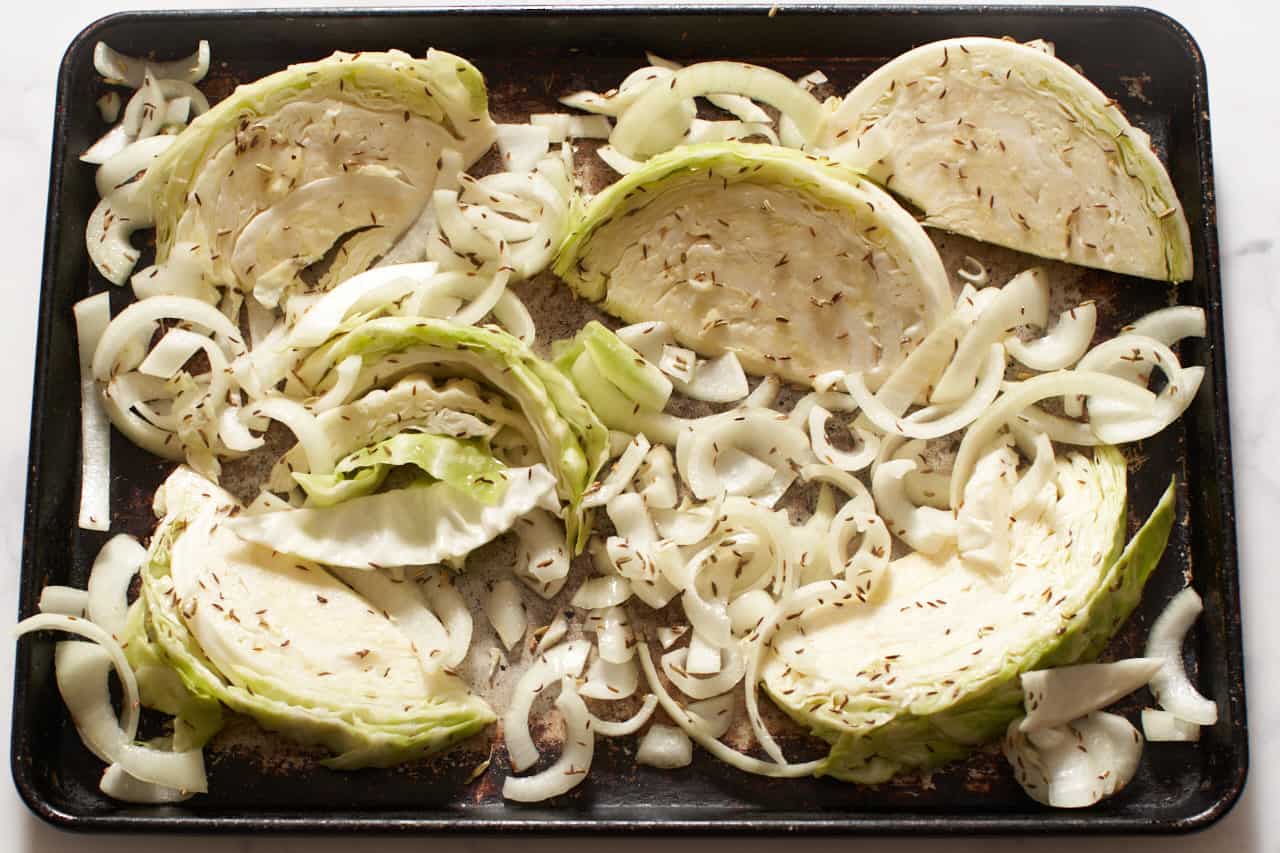 Cabbage wedges and onions seasoned with spices on a sheet pan.