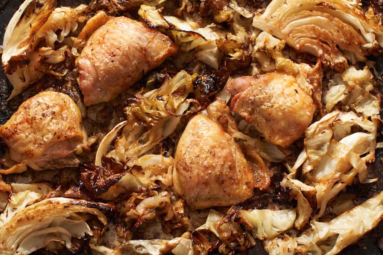 Roasted cabbage and chicken thighs with onions on a sheet pan.