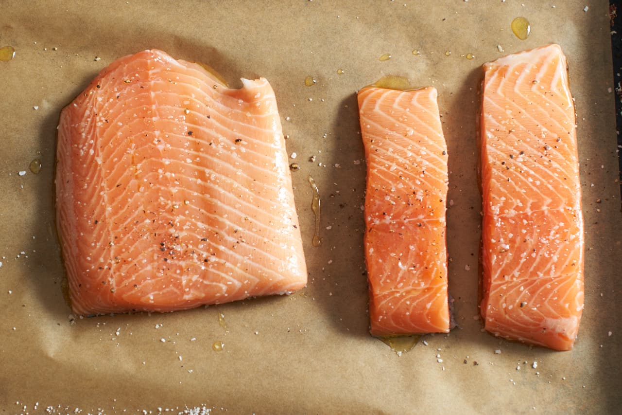 Three pieces of raw salmon seasoned with salt and pepper on a parchment lined baking sheet.