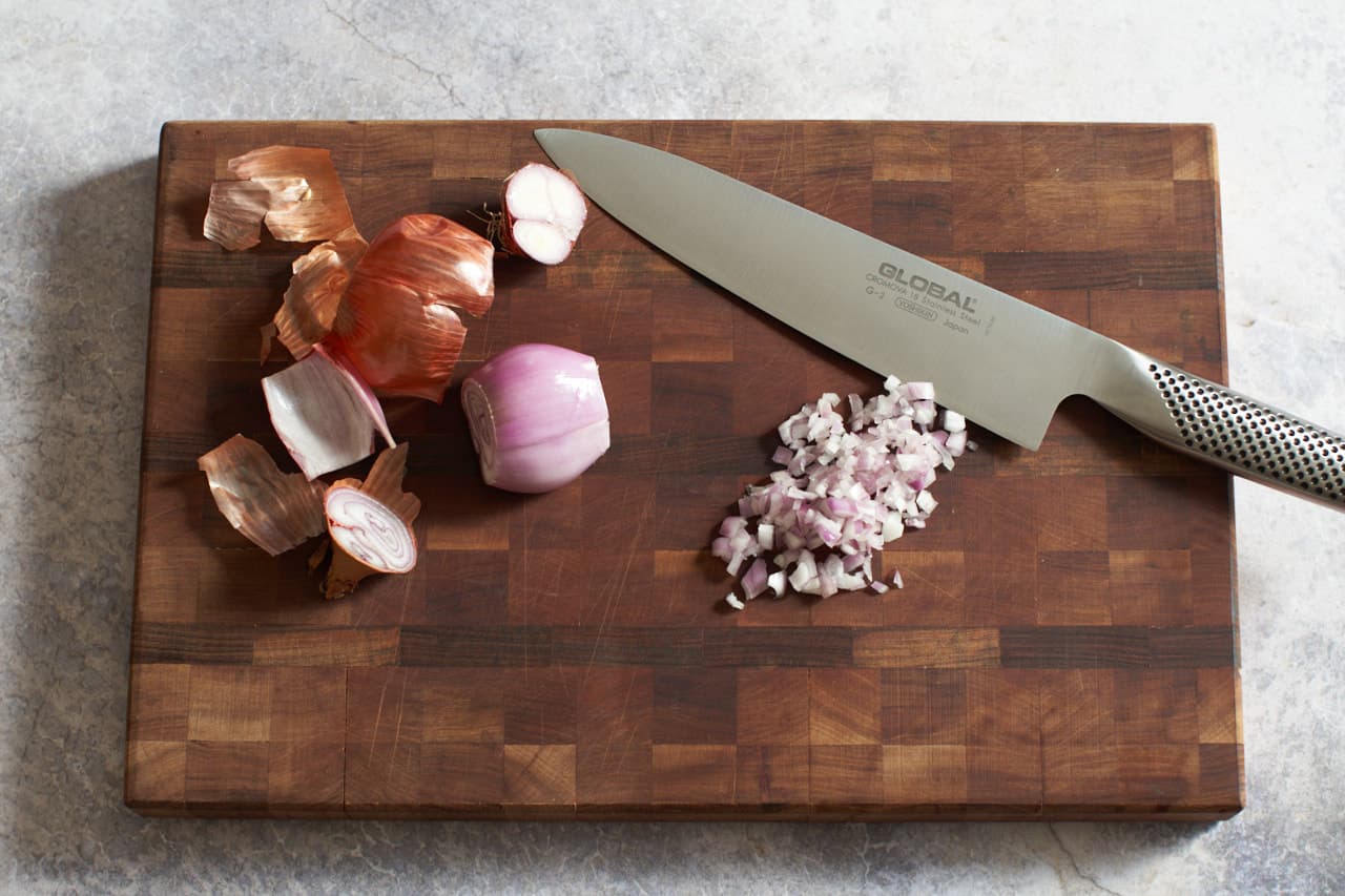 A knife on a cutting board with diced shallots.