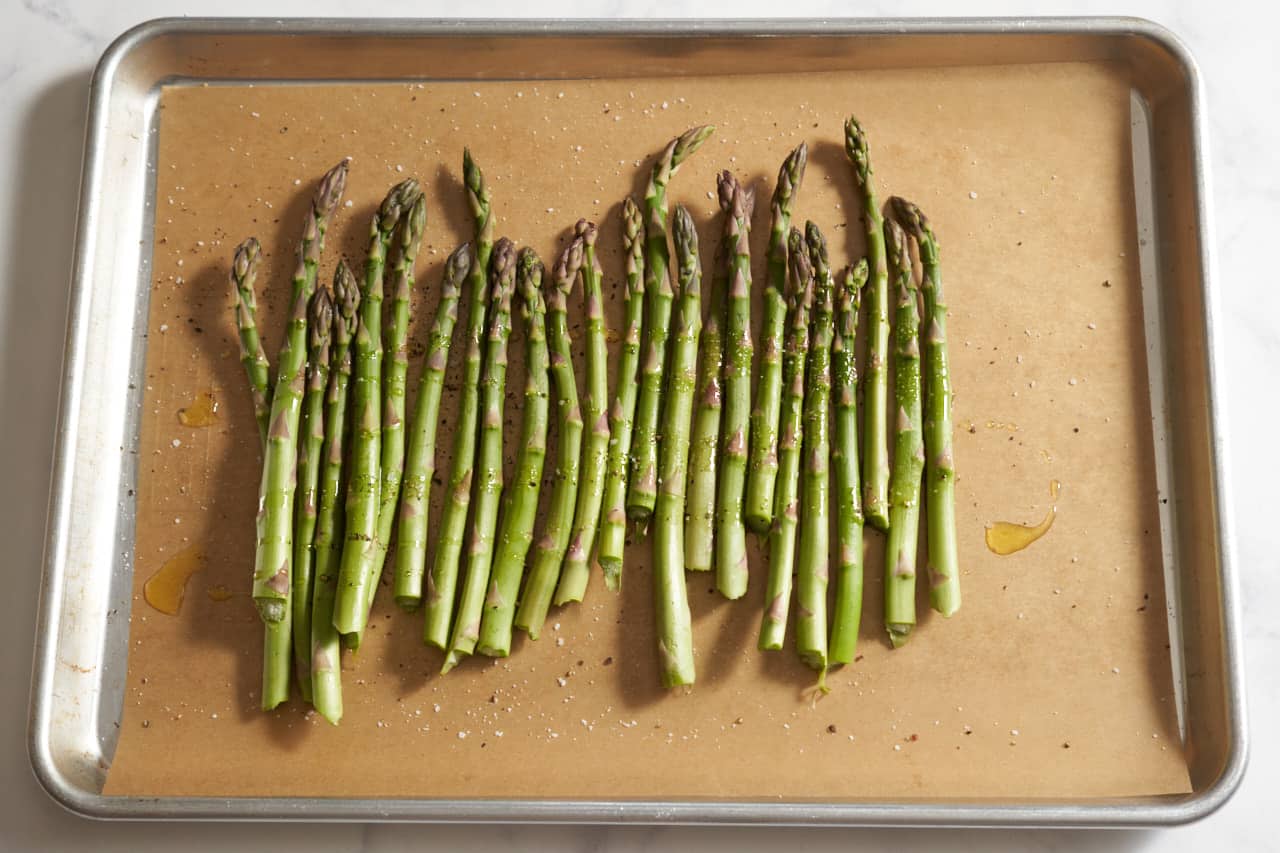 Raw asparagus on a parchment lined sheet pan with olive oil, salt, and pepper.