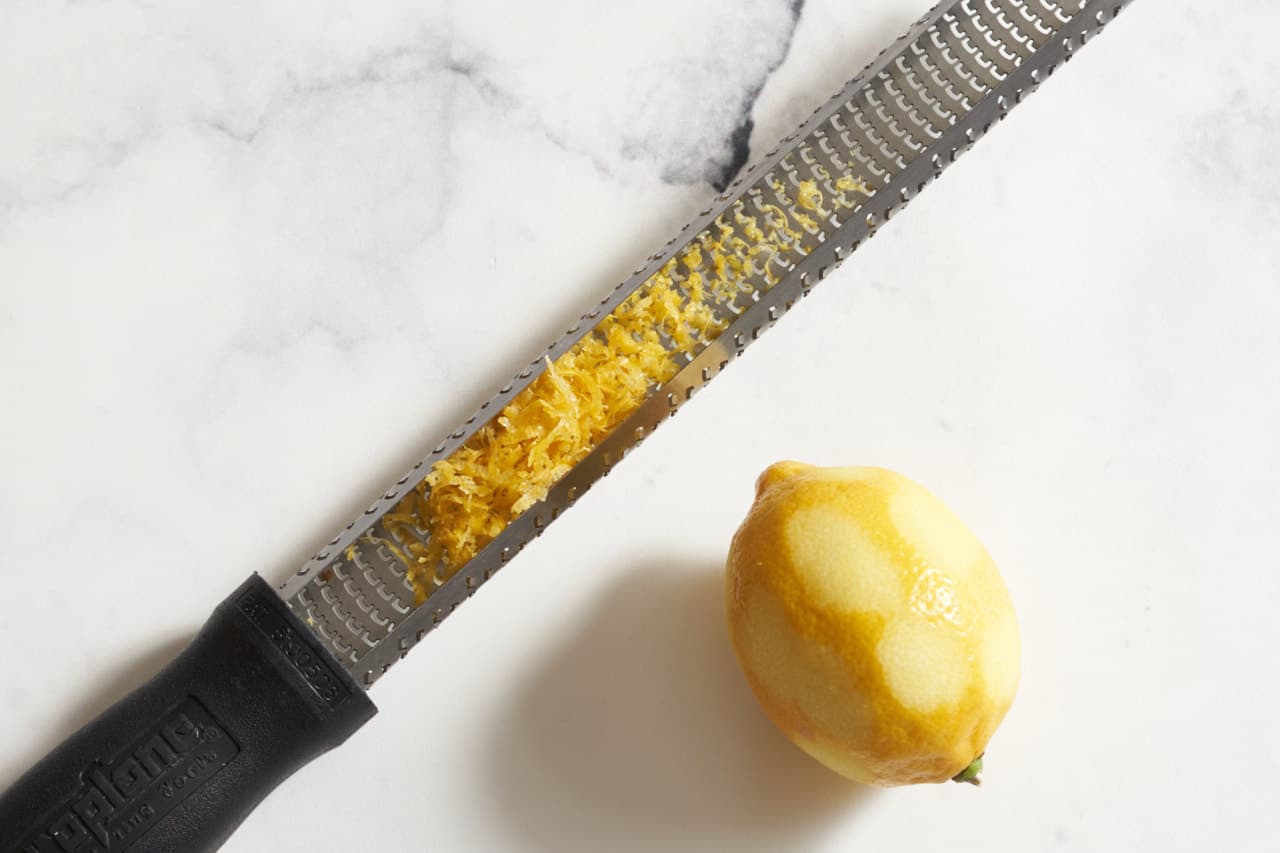 A microplane grater with lemon zest next to a lemon that has been zested.
