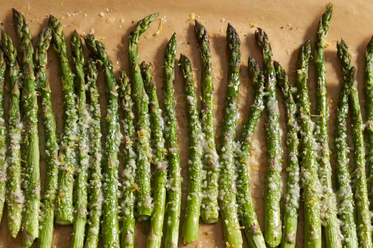 Baked asparagus with parmesan cheese topped with lemon zest on parchment paper.