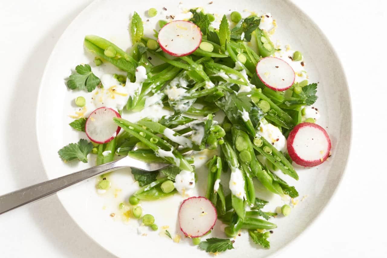 A fork on a plate of sugar snap pea salad.