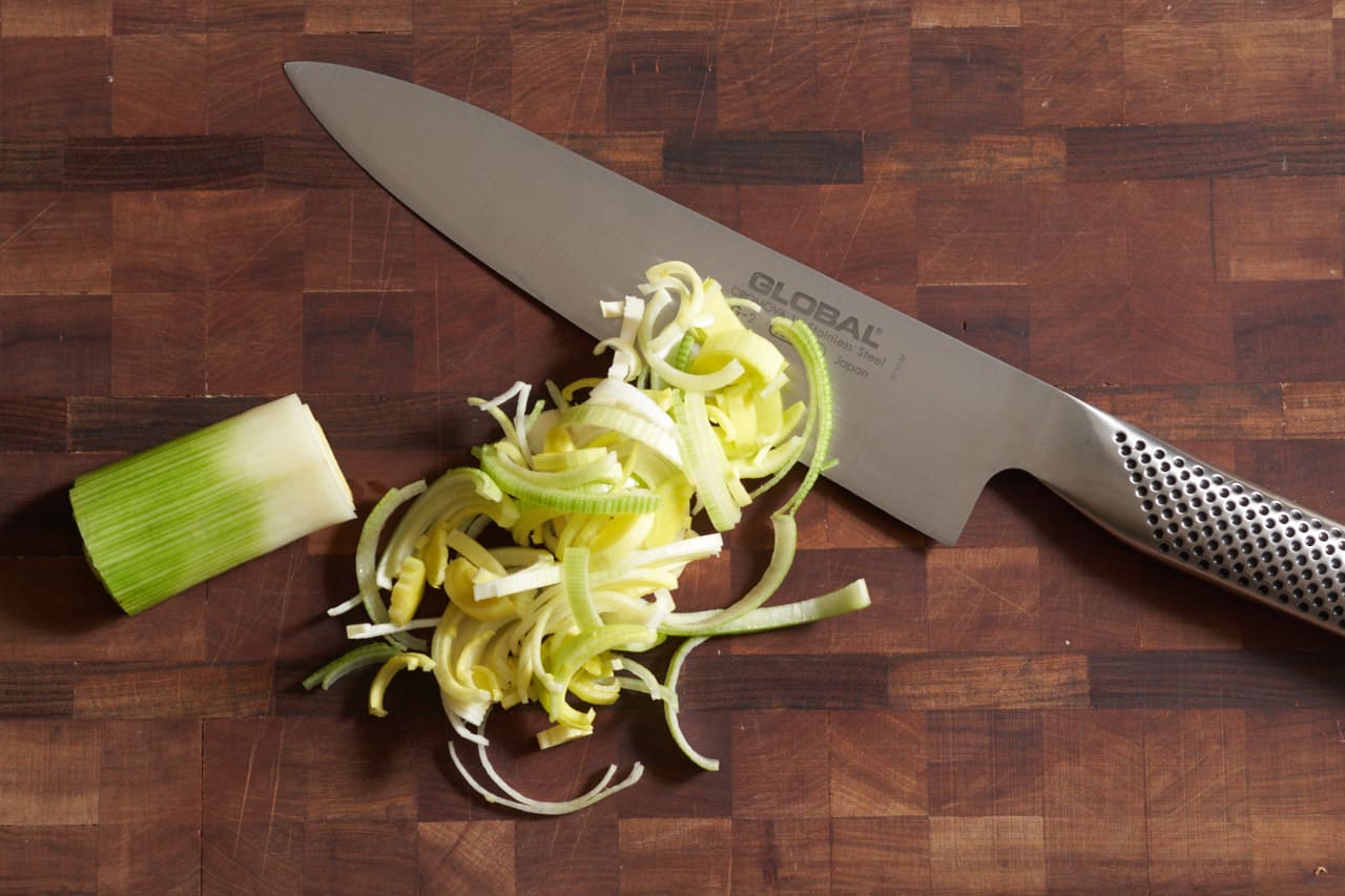A knife on a cutting board with thinly sliced leeks.