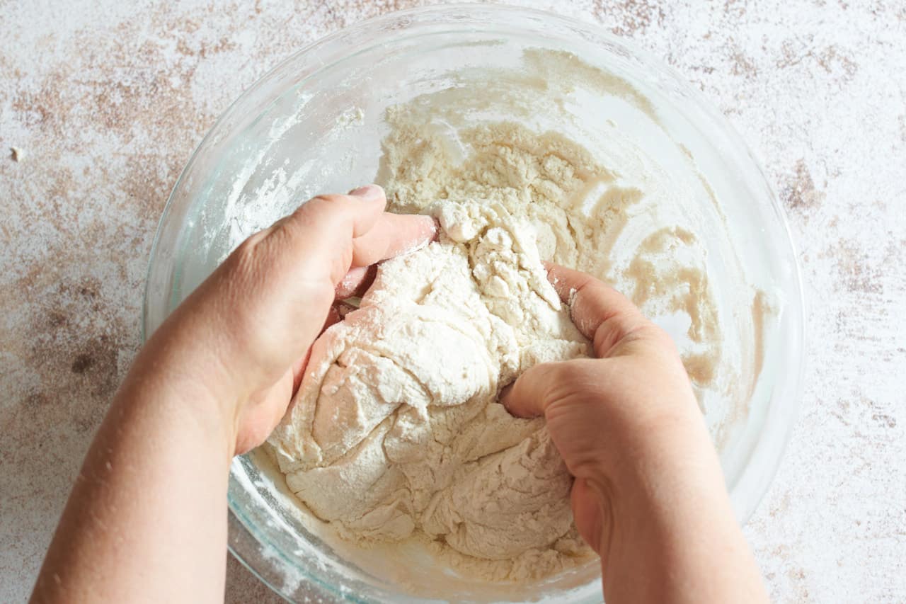 A woman's hands are working flour into pampushky dough starter.