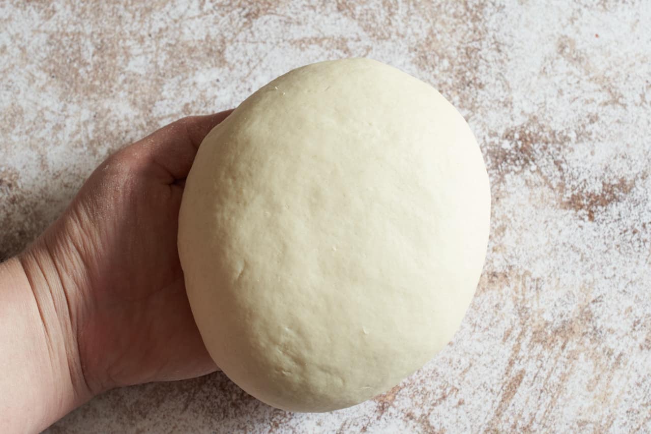 A woman's hand holds a ball of dough that is smooth from kneading.