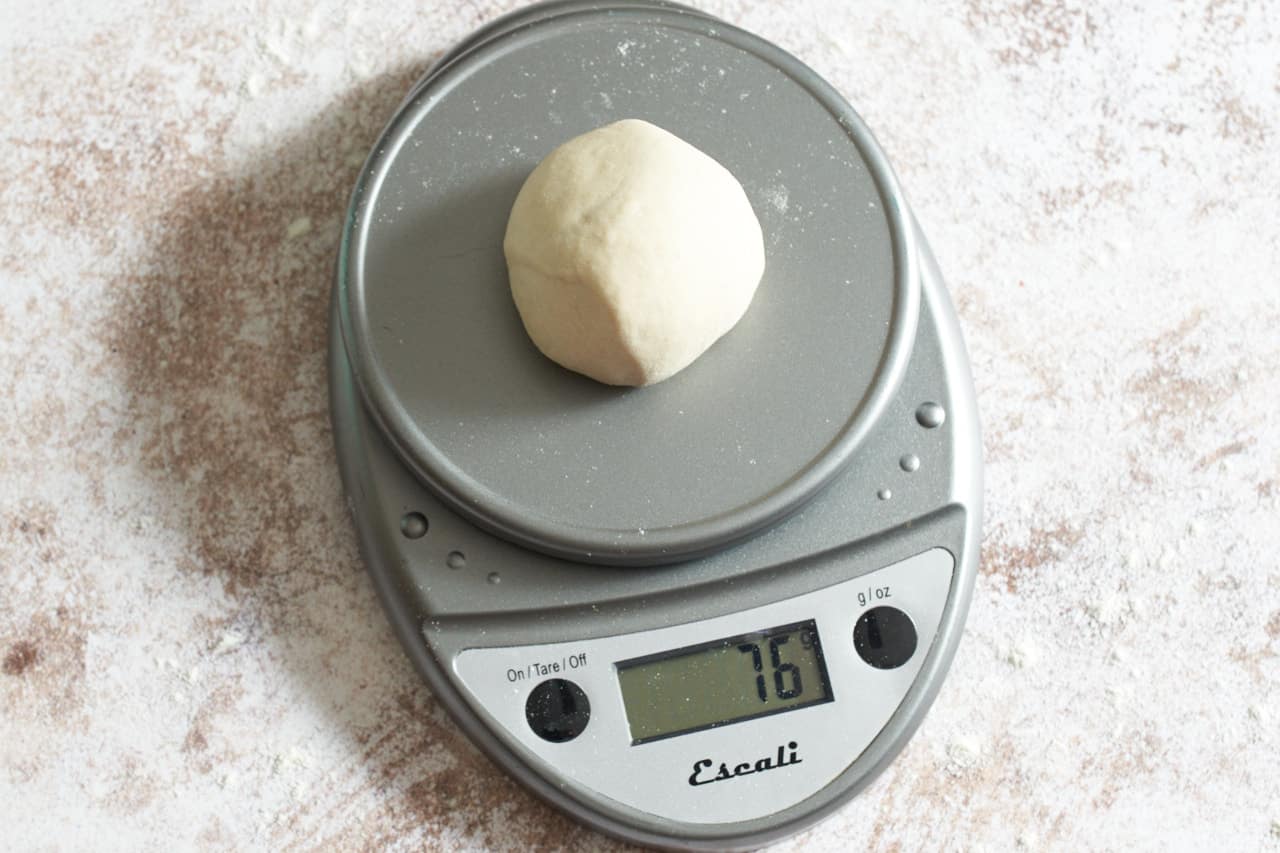 A ball of dough being weighed on a kitchen scale.