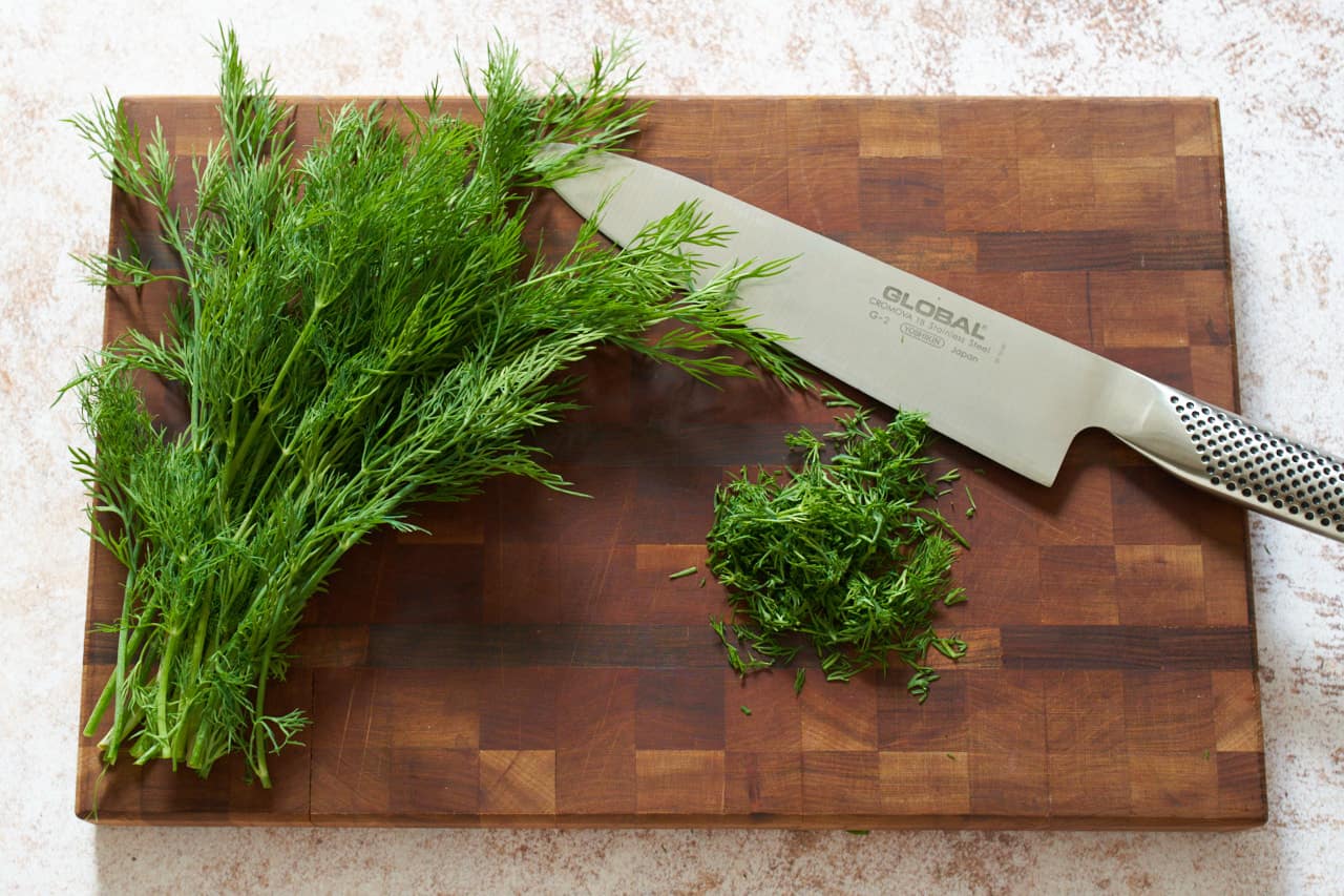 Fresh dill on a cutting board with a knife.