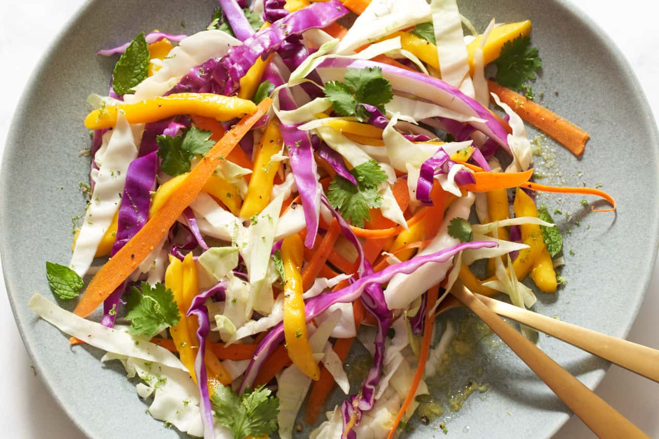 A plate of mango slaw with two gold utensils on it.