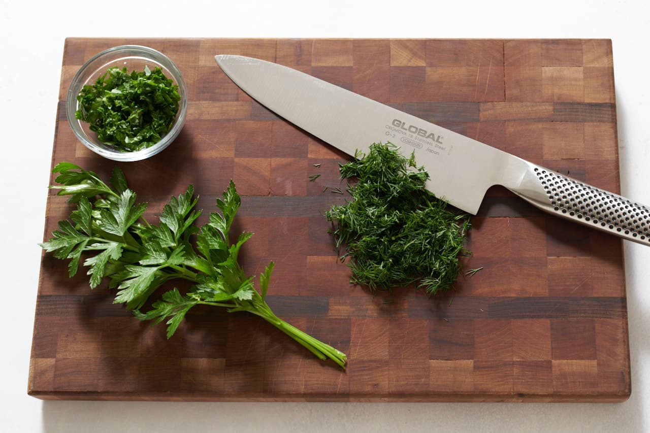 Chopped dill and fresh parsley on a cutting board with a knife.